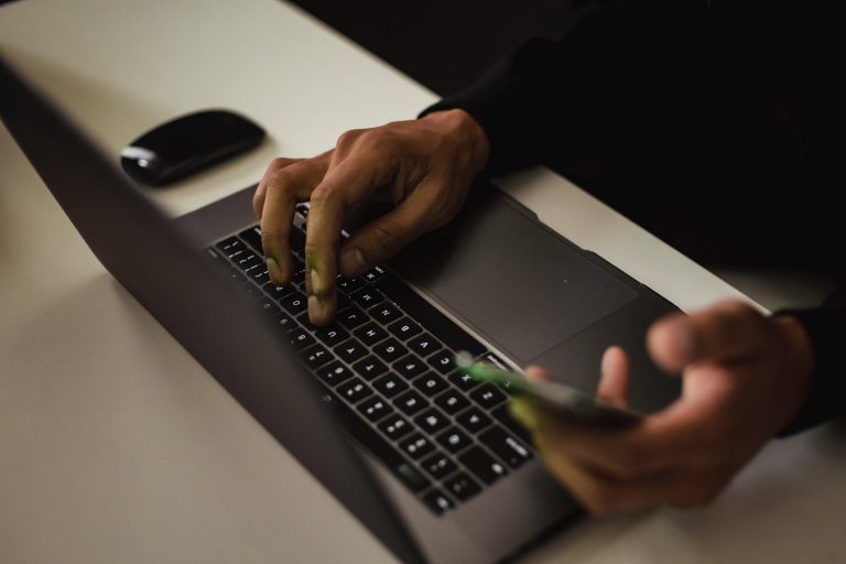 crop faceless man typing on laptop and using smartphone